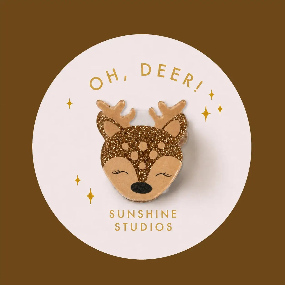 A circular hair clip featuring a cute sleeping deer head with gold glitter antlers and a black nose, set against a white circle with the text 'OH, DEER!' and 'SUNSHINE STUDIOS' in gold.