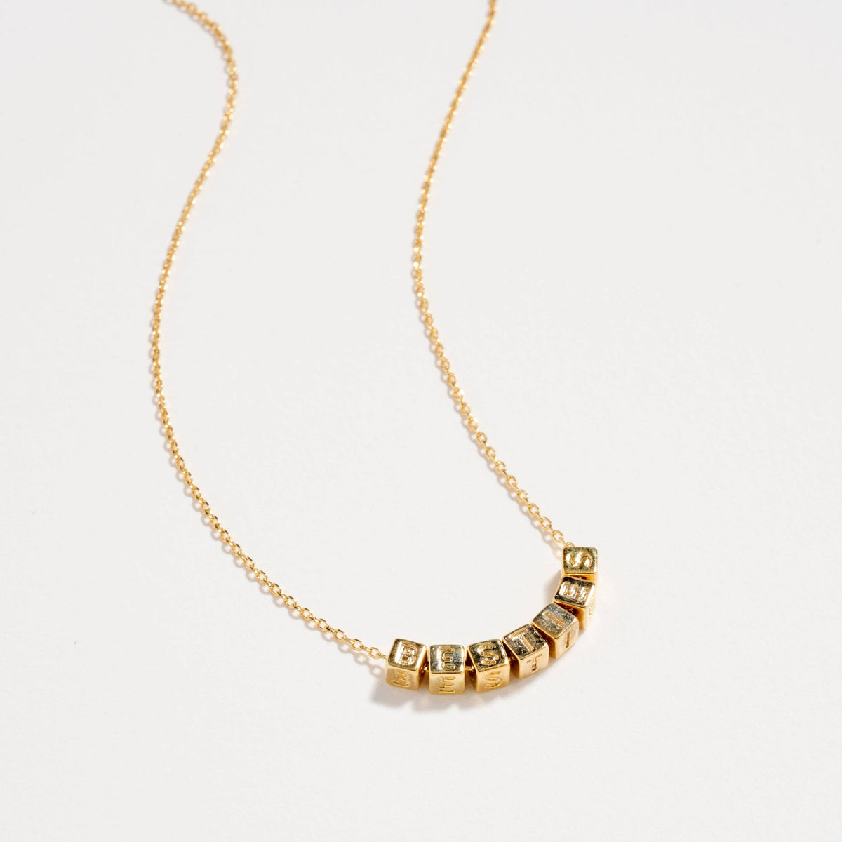A delicate gold chain necklace featuring a curved row of small, square gold pendants, each set with a tiny clear gemstone, displayed on a clean white background.