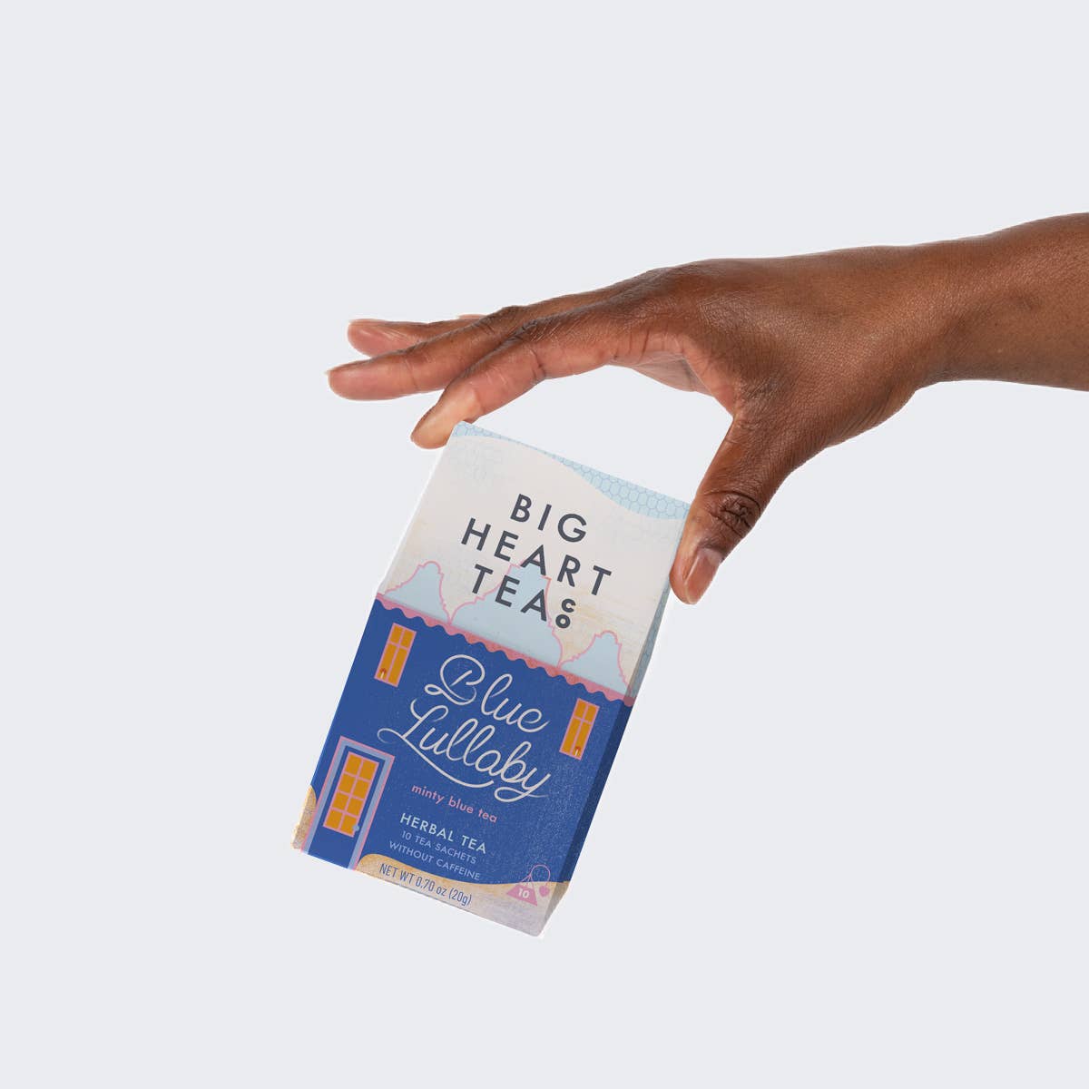A hand holding a box of Big Heart Tea Blue Lullaby herbal tea against a light gray background.
