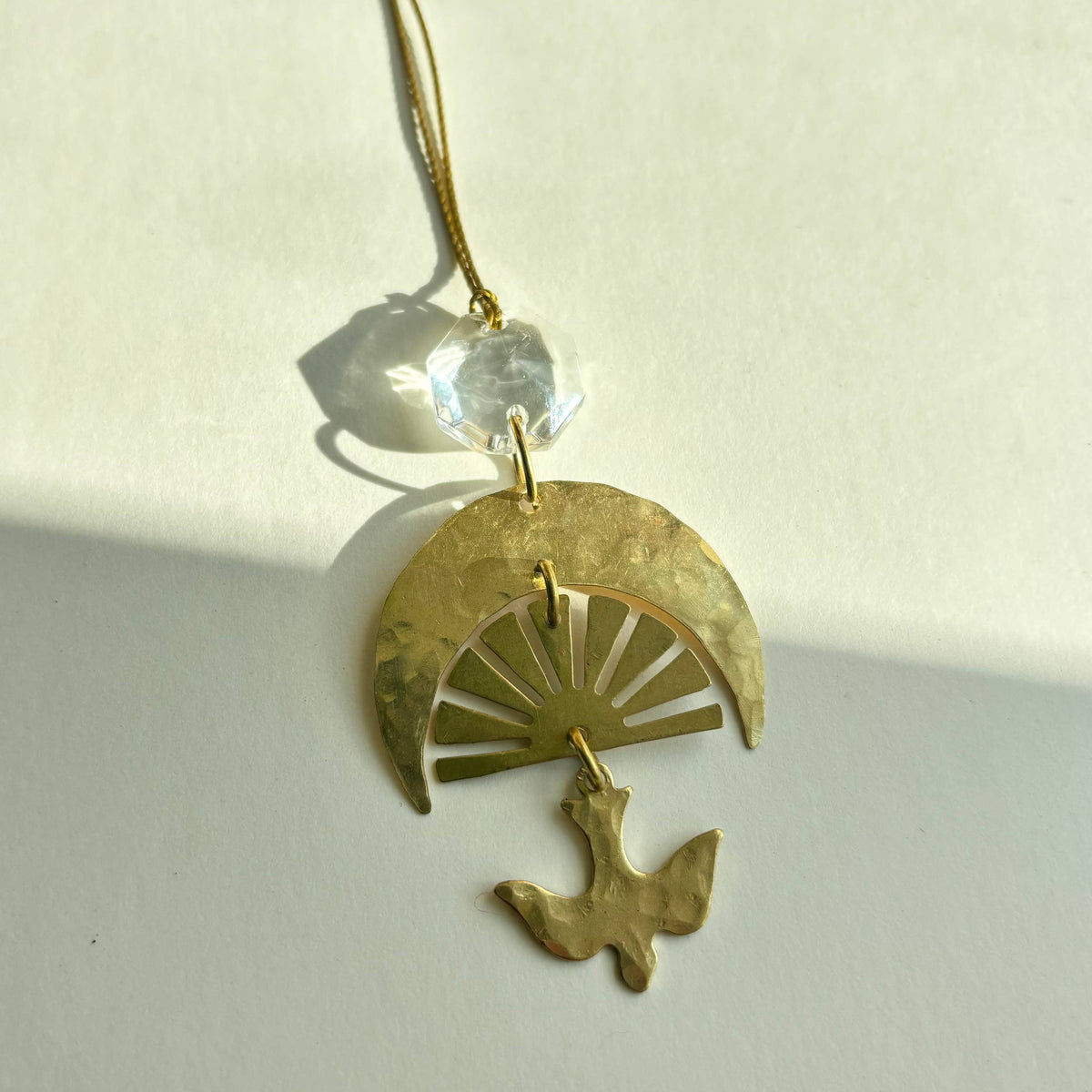 Gold pendant with a crescent moon and bird design on a white background