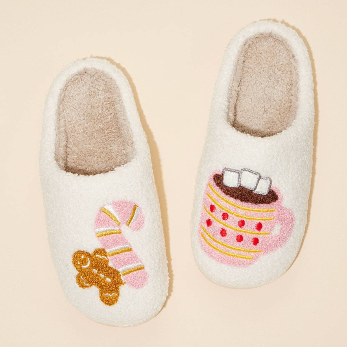 Pair of slippers with candy cane, gingerbread, and hot cocoa on a beige background