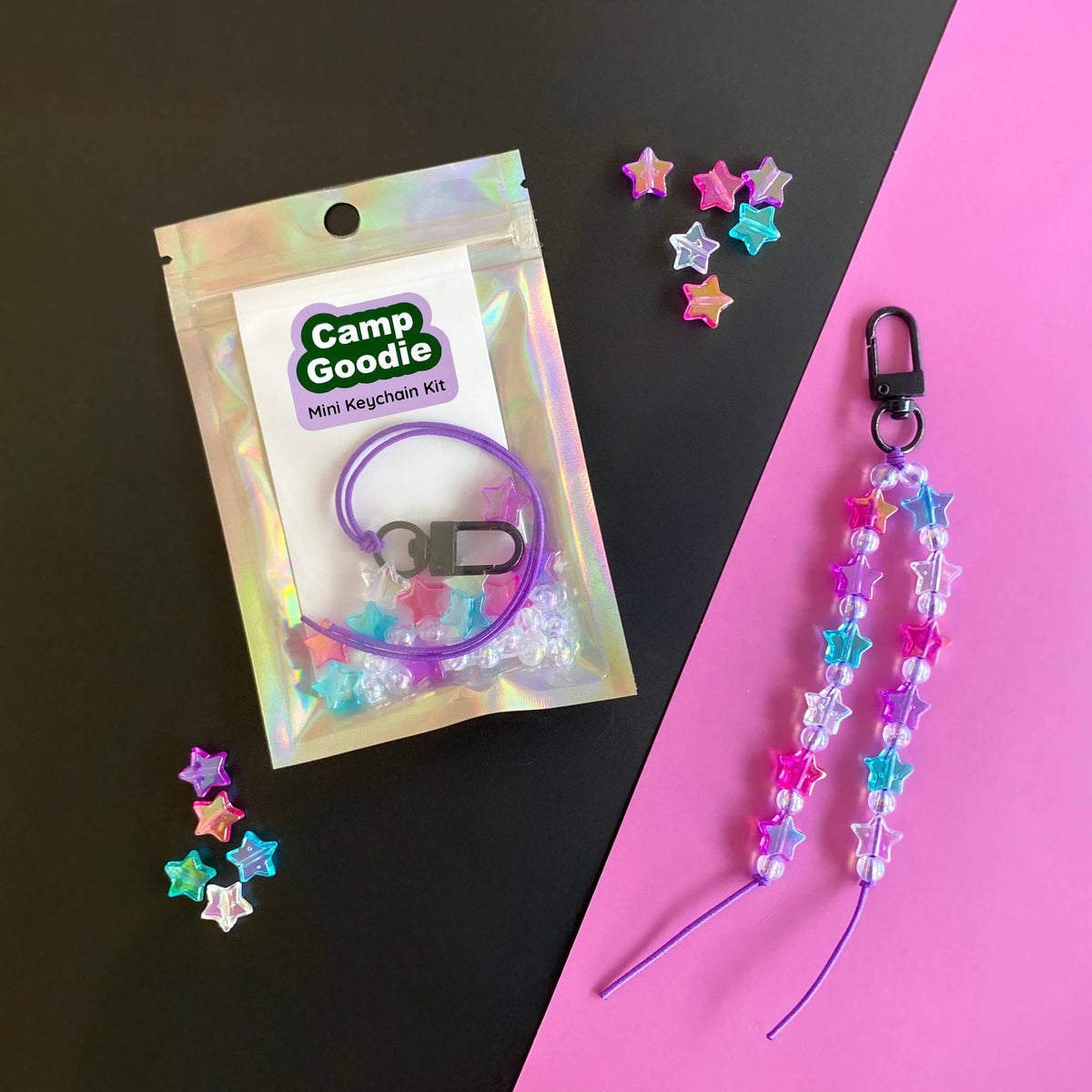 A Camp Goodie mini keychain kit shown in its holographic pouch next to a completed keychain made of colorful star beads on a pink and black background.