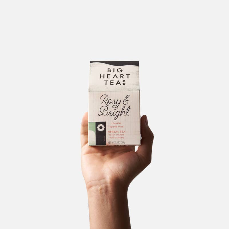 Hand holding a box of 'Big Heart Teas' Rosy & Bright tea against a white background