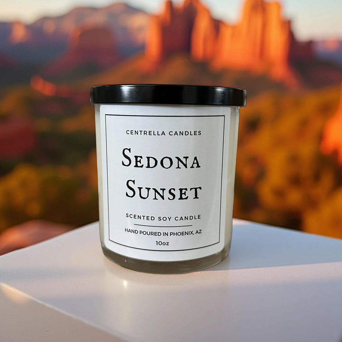 A glass jar candle with a black lid and a white label reading 'Centrella Candles Sedona Sunset Scented Soy Candle' background.