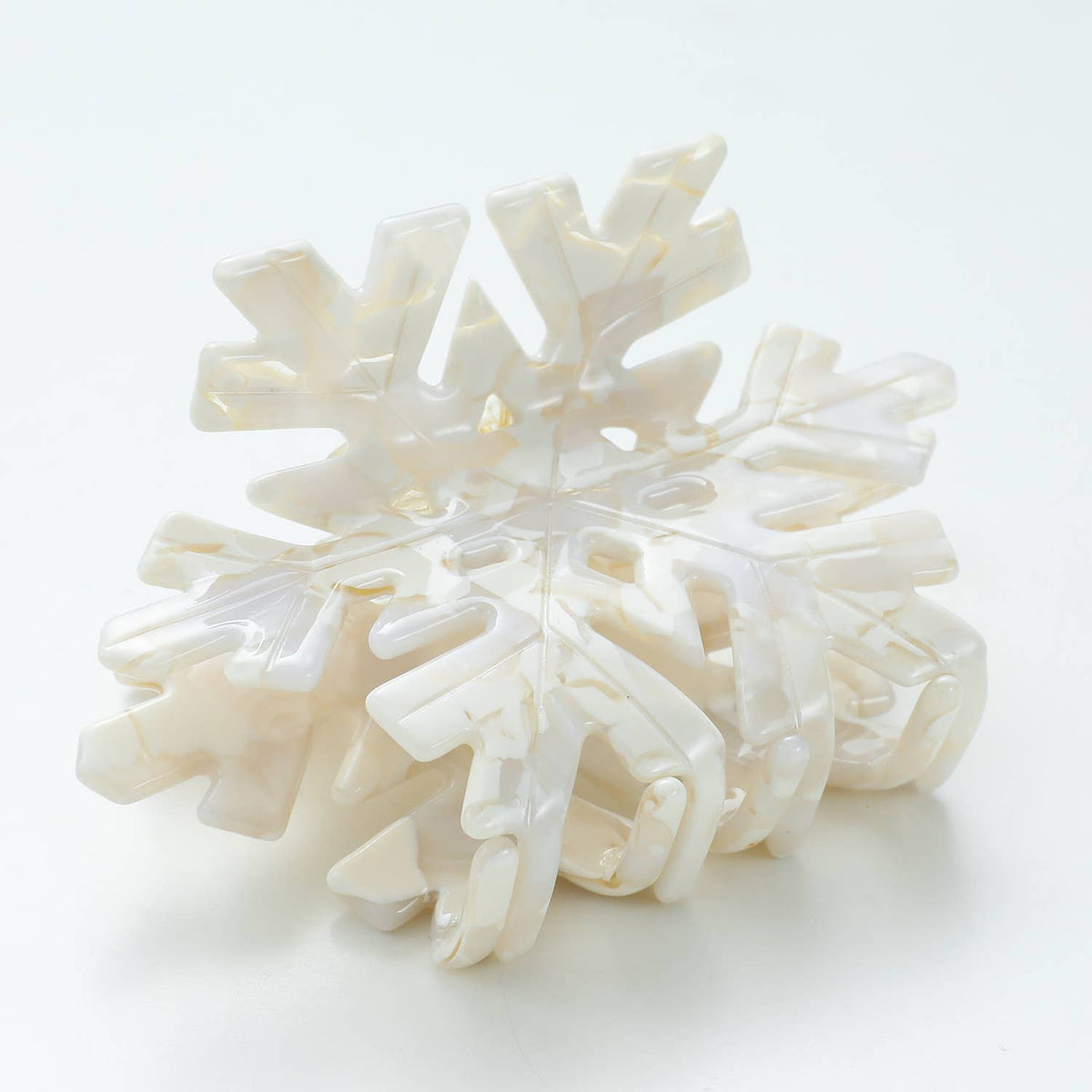A translucent snowflake-shaped decorative claw clip made from layered, glossy white and cream shell-like material, photographed on a clean white background.