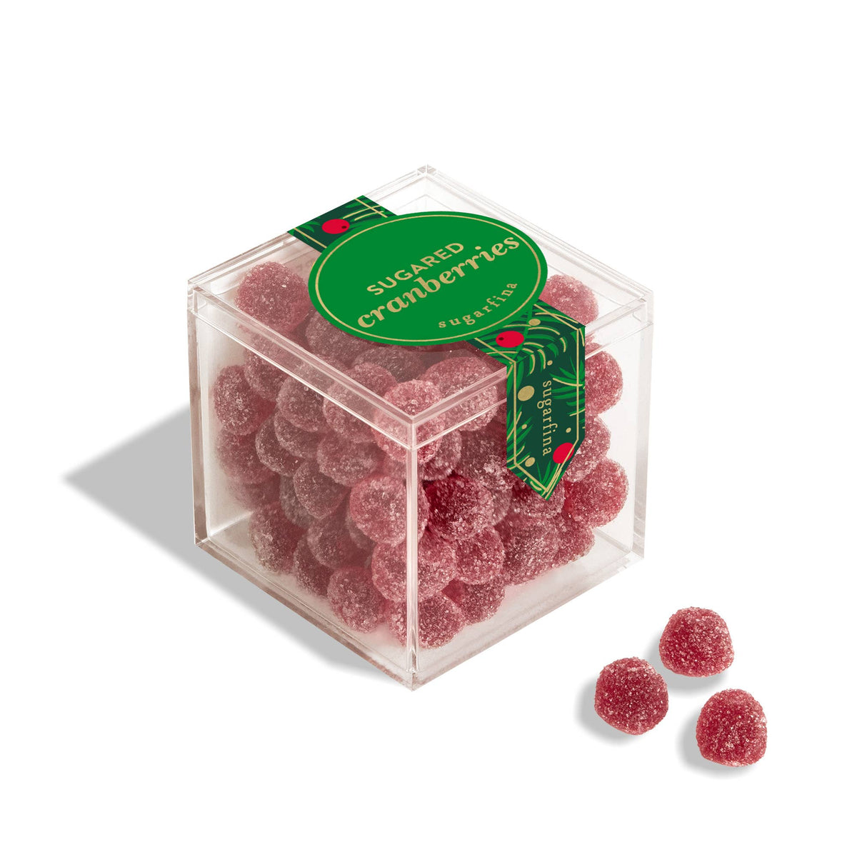 A clear square plastic box filled with round, sugar-coated red cranberry candies, with a green circular label reading 'SUGARED cranberries' and three loose candies placed in front on a white background.
