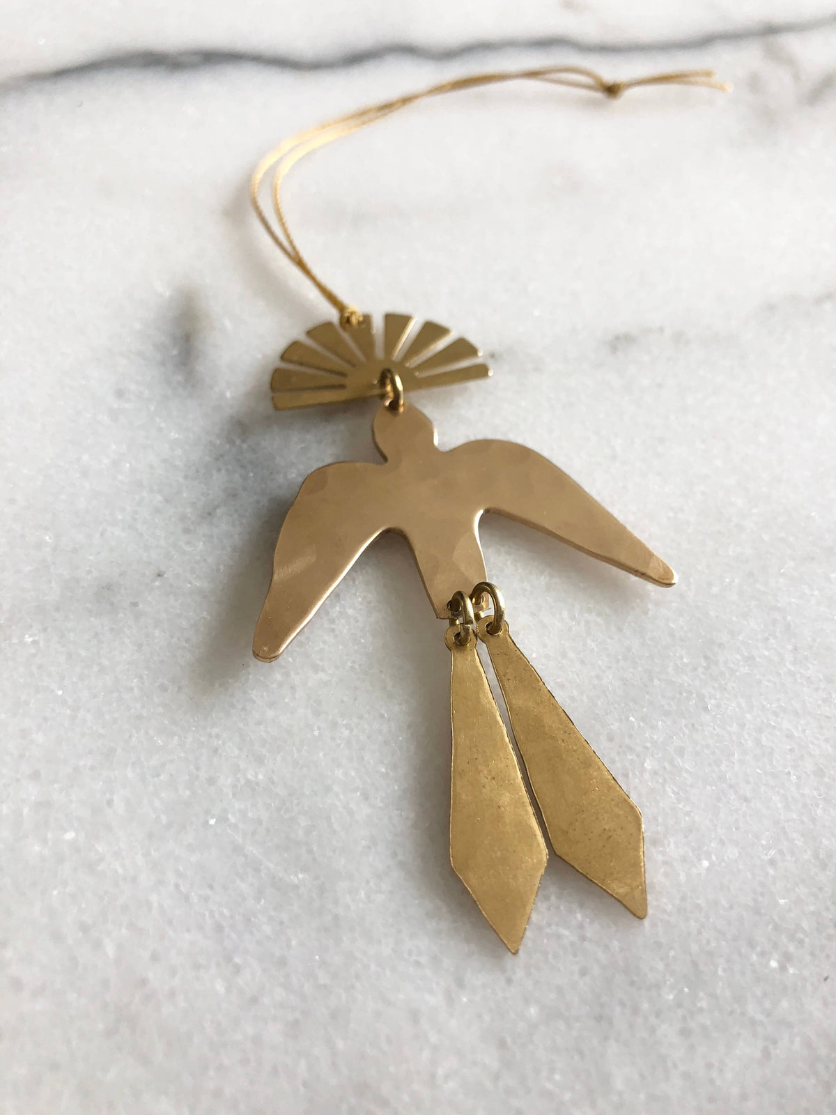 Gold bird-shaped pendant ornament on a marble surface