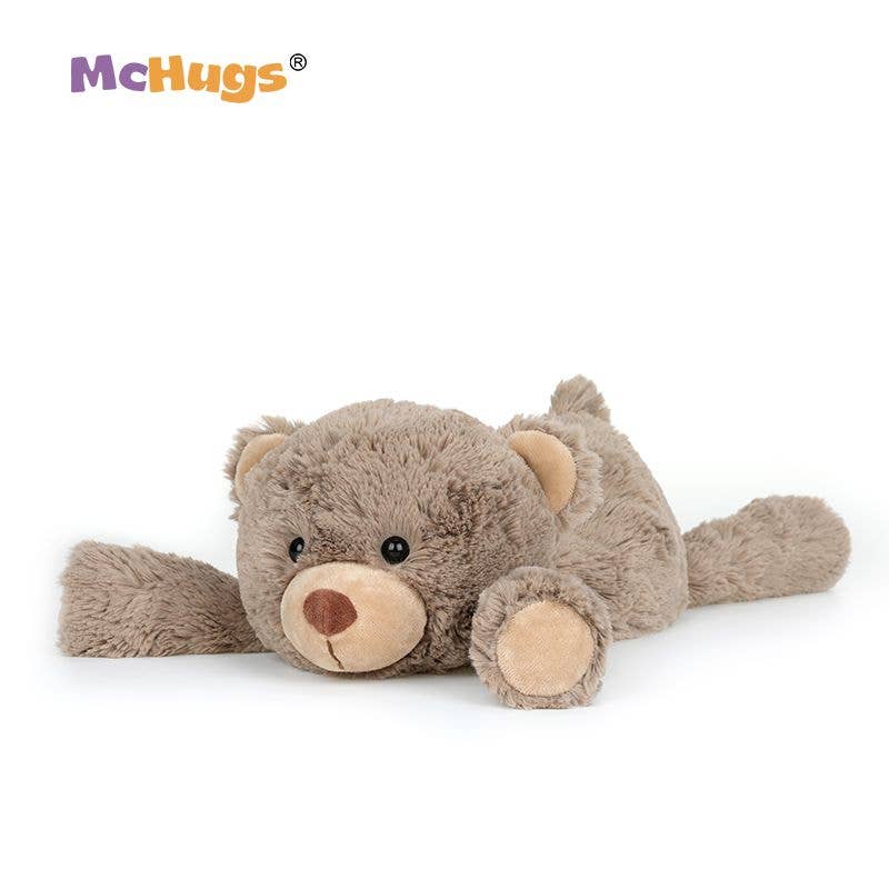 A plush teddy bear toy lying on its side, made of soft taupe-brown fabric with a lighter beige snout, inner ears, and paw pads. The toy has small black bead eyes and a stitched nose.